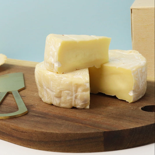 Three blocks of cheese on a wooden board with a knife, against a light blue background.