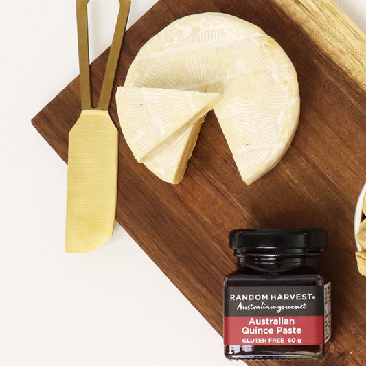 Wooden board with cheese, nuts, and a jar of jam, tied with a black ribbon on a white background.