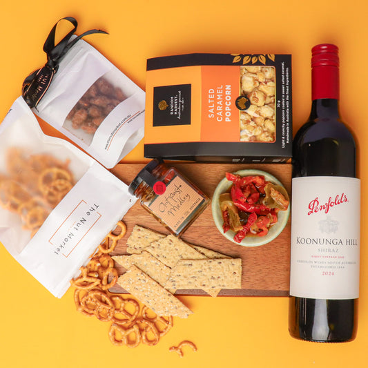 Gourmet snack and wine set with pretzels, popcorn, crackers, and a bottle of wine on a yellow background.