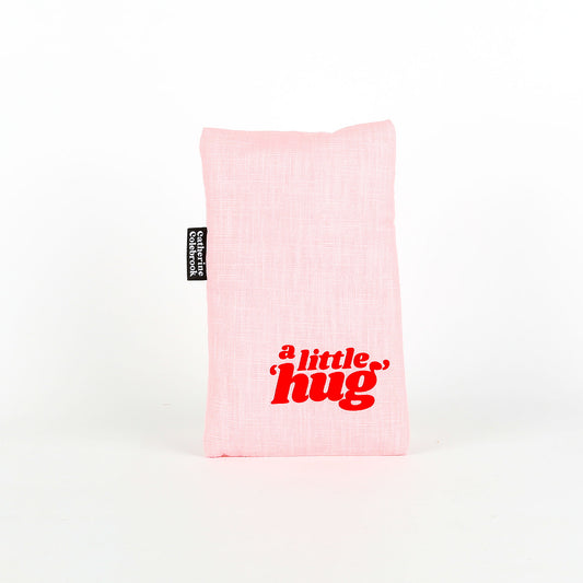 Pink heat pack with 'a little hug' text on a white background