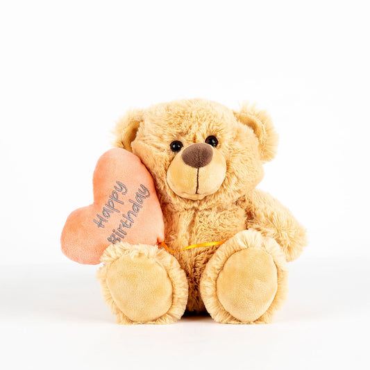 Plush teddy bear holding a heart with 'Happy Birthday' text written on it on a white background