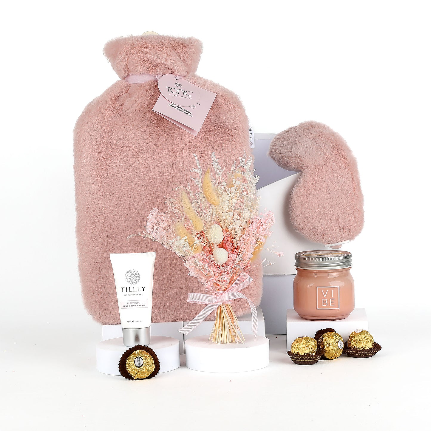 Pink hot water bottle, mittens, flowers, cream, and chocolates on a white background