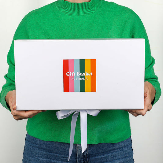 Person holding a white gift box with colorful Gift Basket Australia label against a plain background