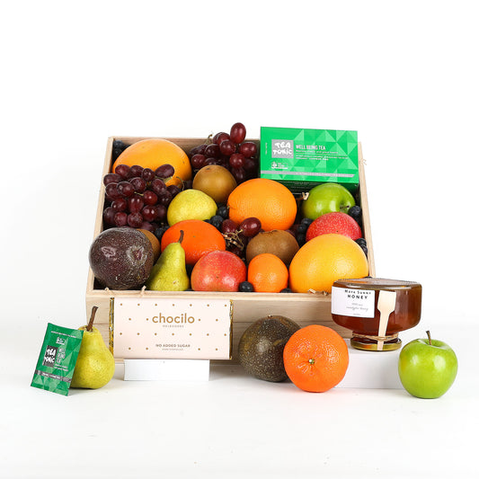 Fruit basket which includes various fruits and a jar of honey on a white background
