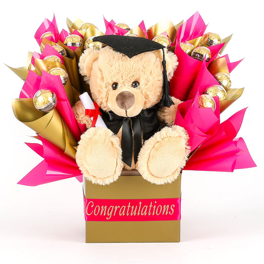 Graduation-themed teddy bear with a bouquet of chocolates wrapped in pink & gold in a box labeled 'Congratulations'.