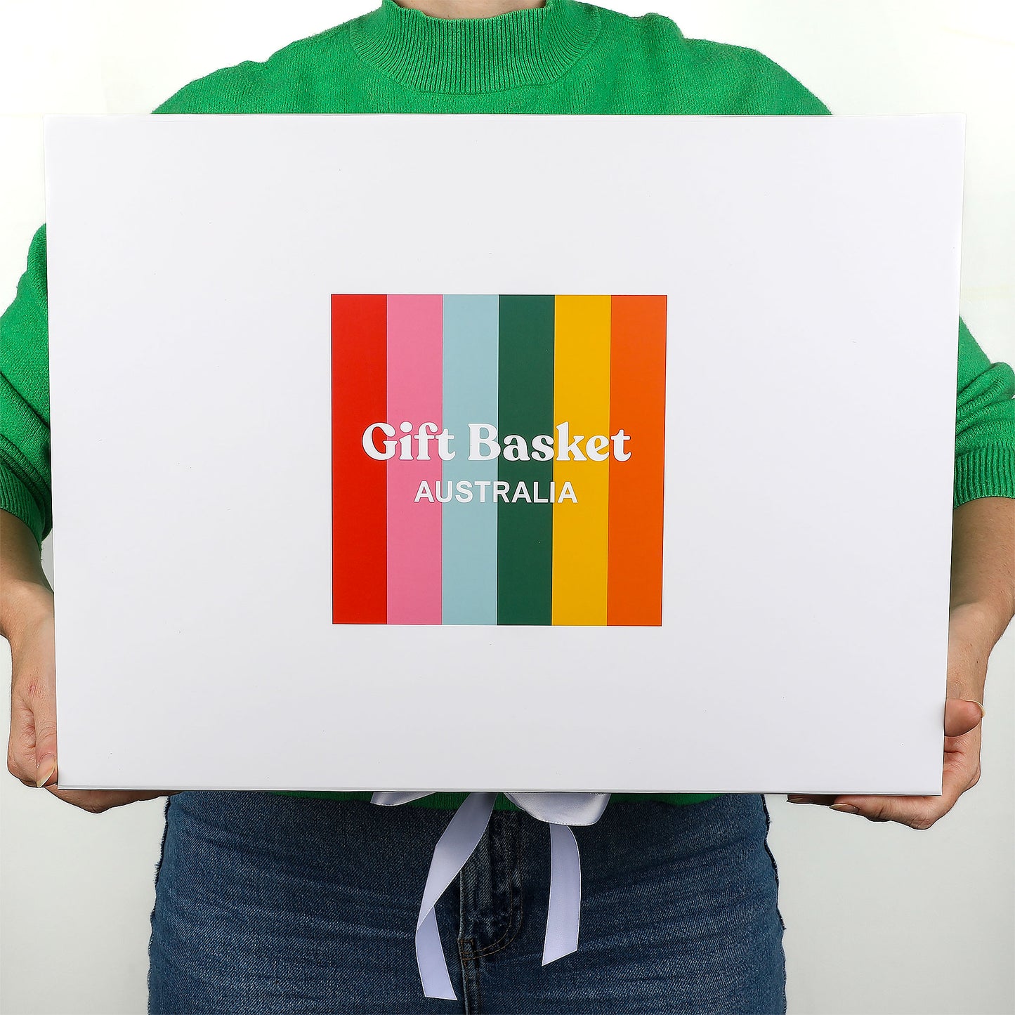 Person holding a white gift box with colorful Gift Basket Australia label against a plain background
