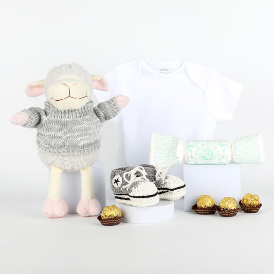 Plush lamb toy wearing a sweater with baby shoes and chocolates on a white background