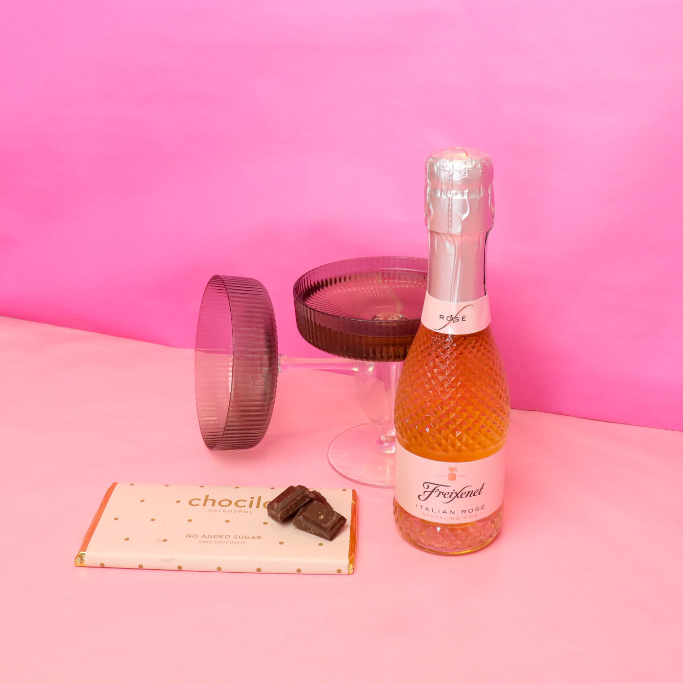 Mini bottle of Freixenet sparkling wine with a glass and chocolate on a pink background