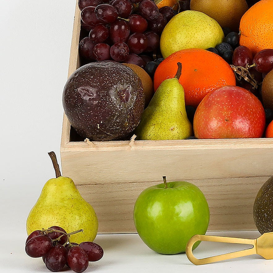 Fruit basket with assorted fruits, Australian Gold chocolate bars, and a cutting board on a white background