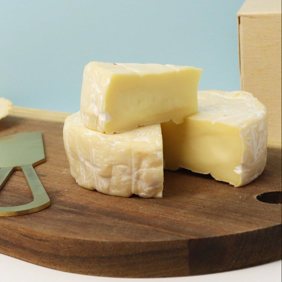 blocks of cheese on a wooden board with a knife, against a light blue background.