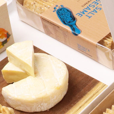 Assorted food items including crackers, cheese, and nuts in a gift box on a white background.