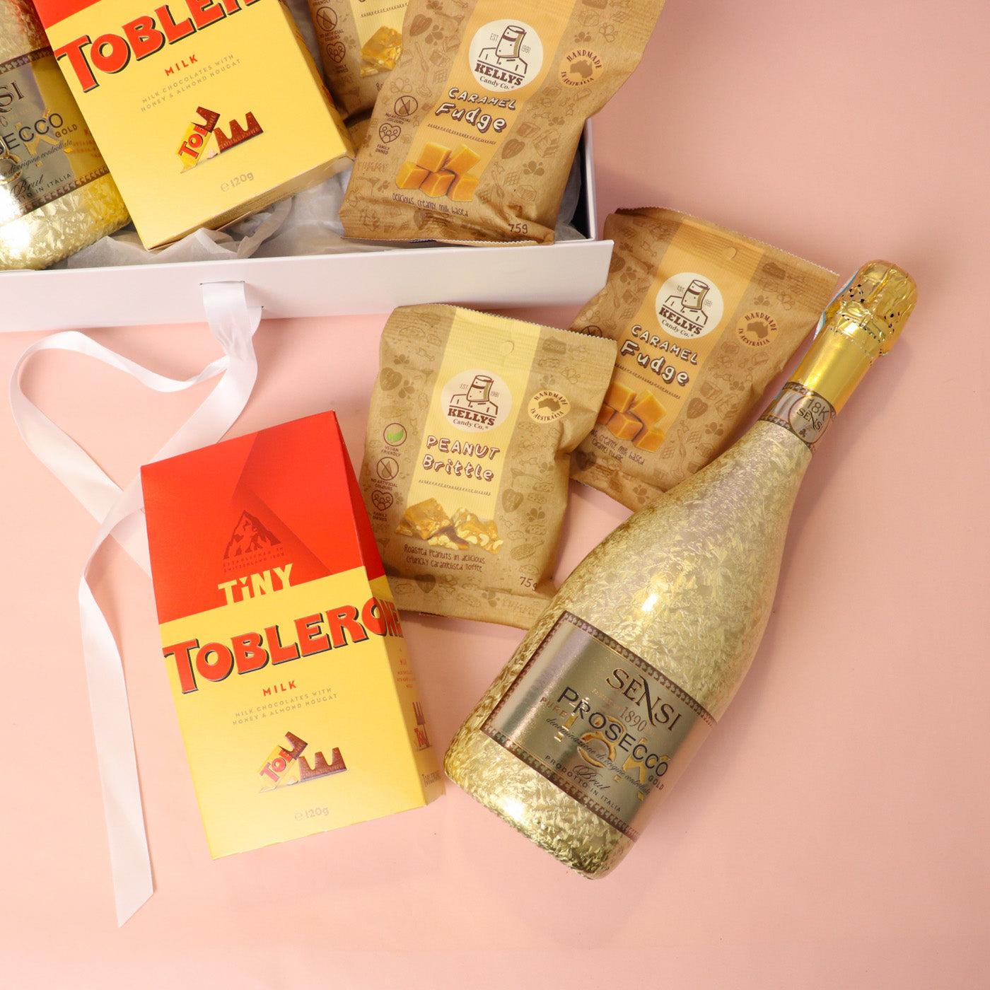 Gold bottle of Prosecco and Toblerone chocolate bars on a pink background