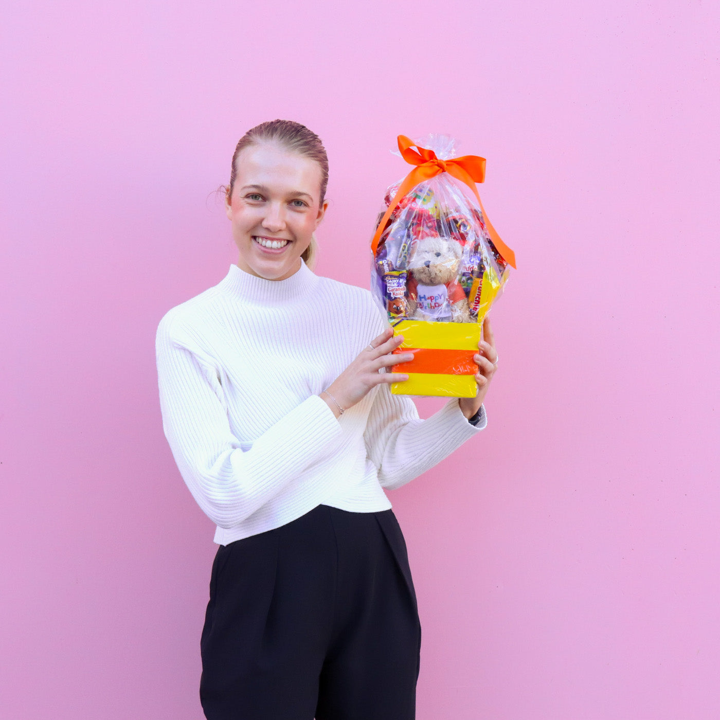 Person holding a gift bag with a teddy bear against a pink background