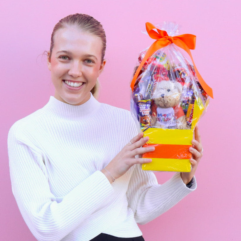 Person holding a gift bag with a teddy bear against a pink background