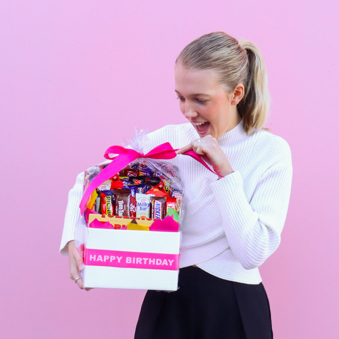 Woman holding a birthday gift basket with a pink background