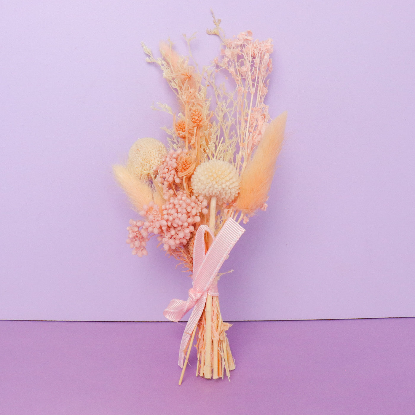 Bouquet of dried flowers with a pink ribbon on a purple background