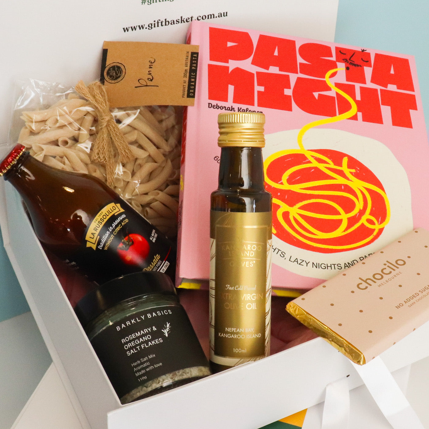 Gourmet gift basket with pasta, olive oil, and chocolate bar on a blue background