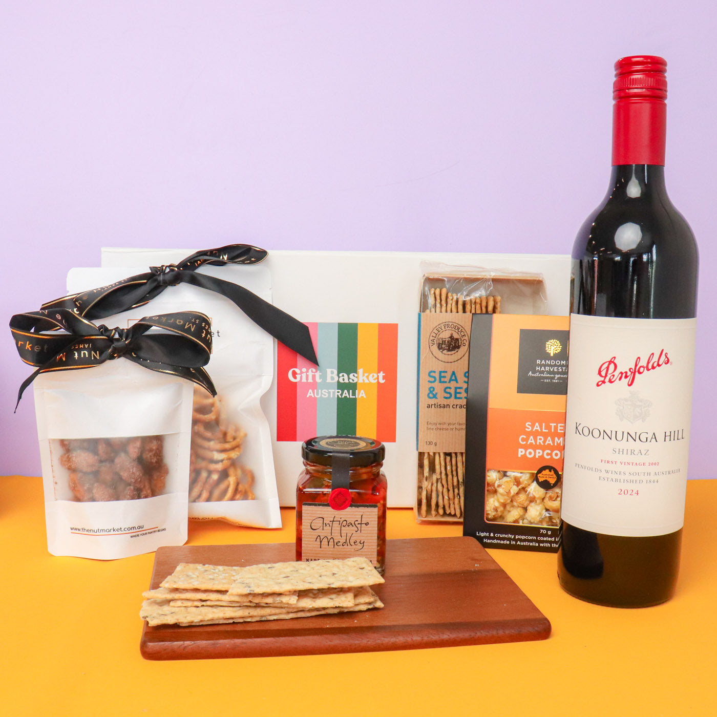Gift basket with wine, snacks, and crackers on a yellow surface with a purple background