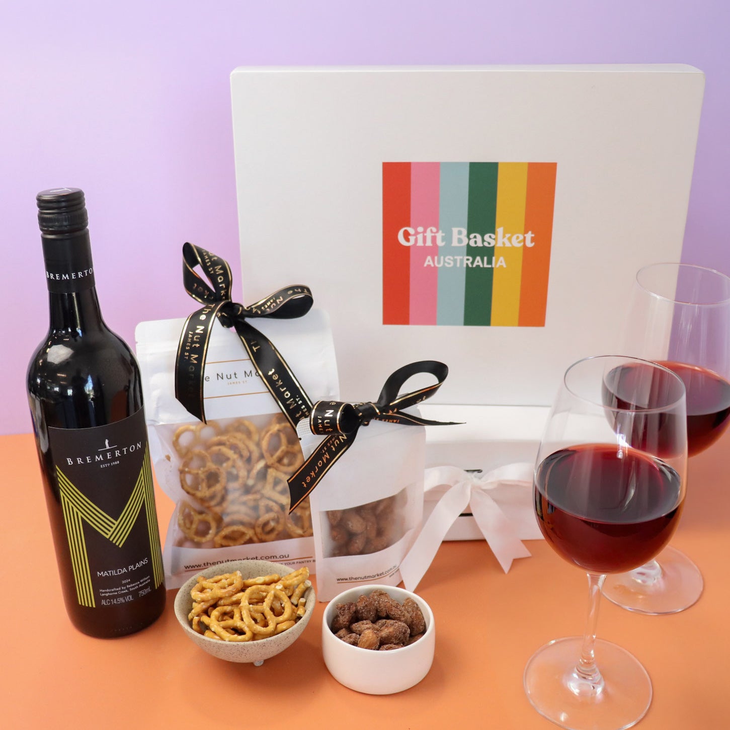Wine bottle, glasses, and snacks with a gift bag on a lilac and orange background
