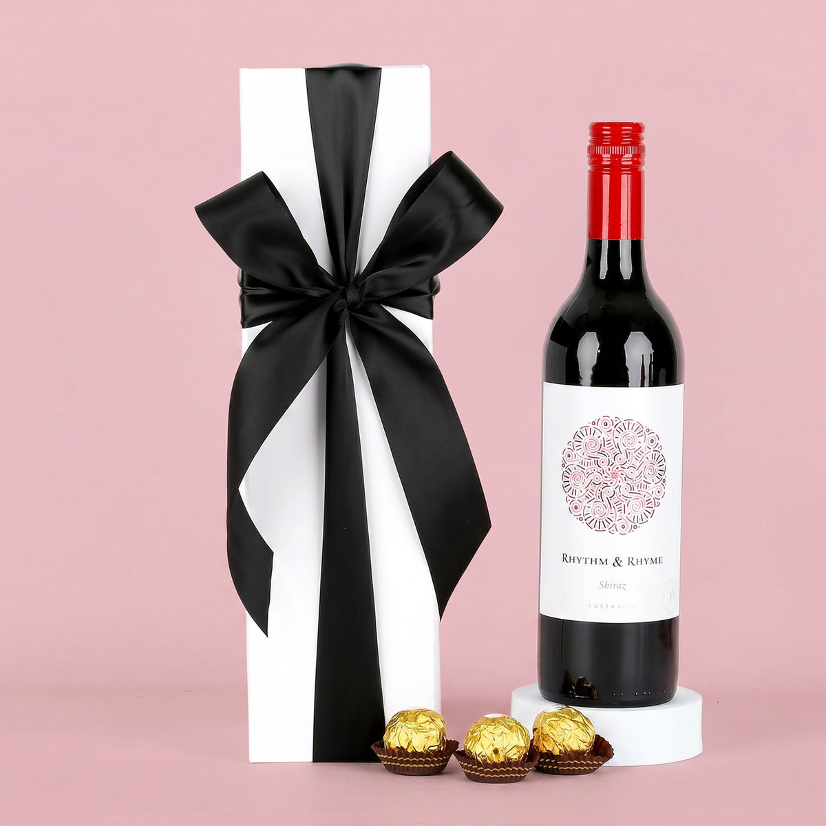 Bottle of red wine with a decorative box and chocolates on a pink background