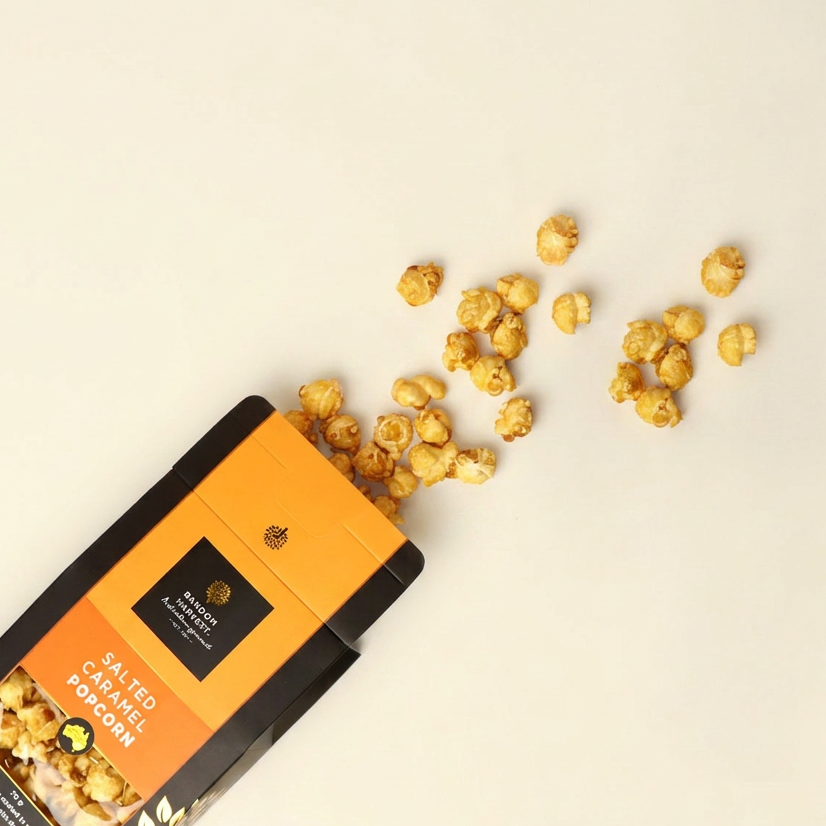 Box of salted caramel popcorn with scattered popcorn on a beige background