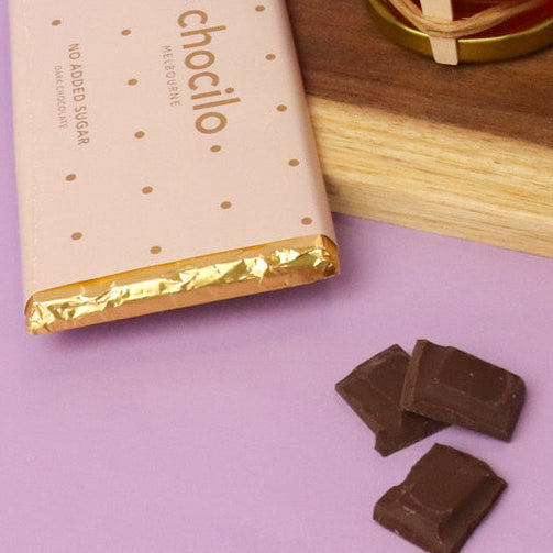 Chocilo chocolate bar with gold foil wrapper and pieces on a pink surface