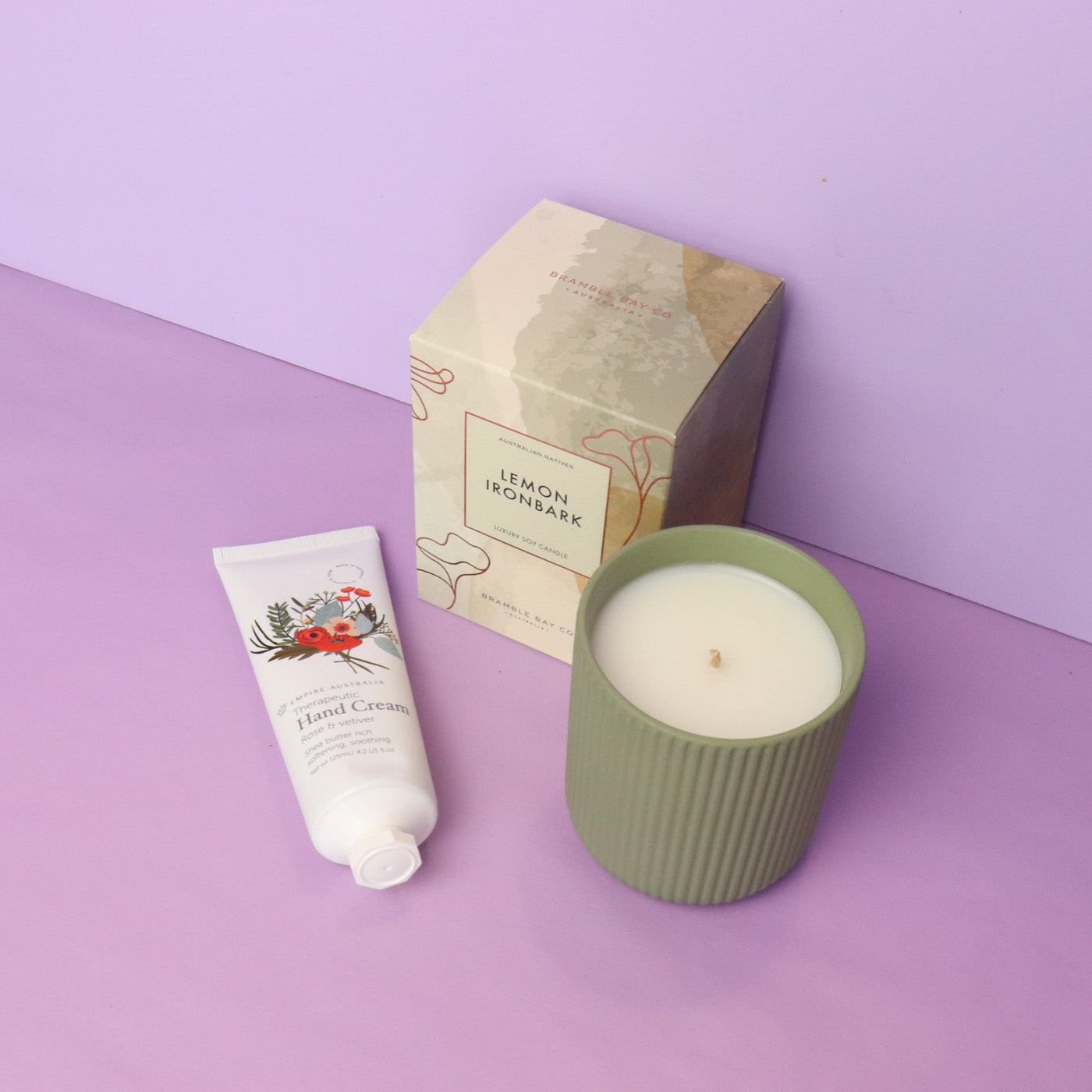 Candle, hand cream, and box on a purple surface