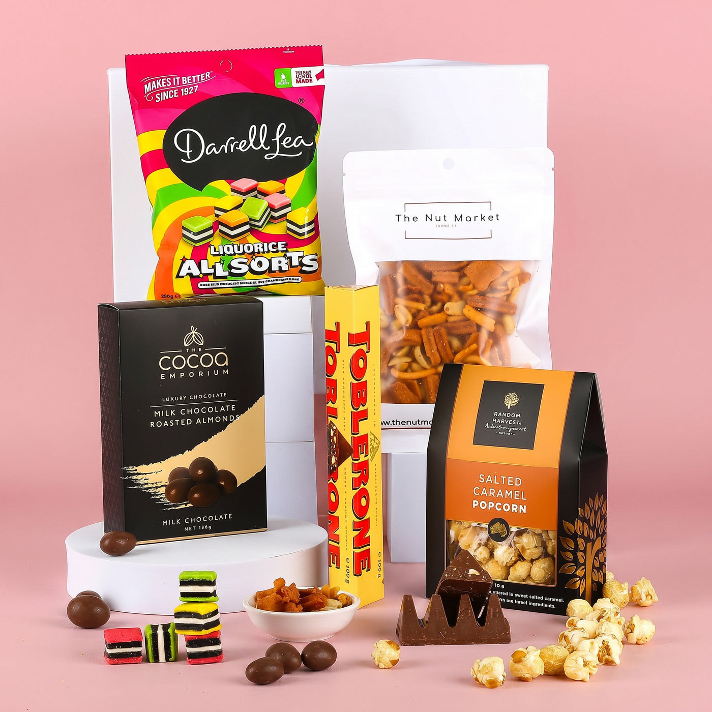 Assorted snacks including liquorice allsorts, chocolate, and popcorn on a pink background