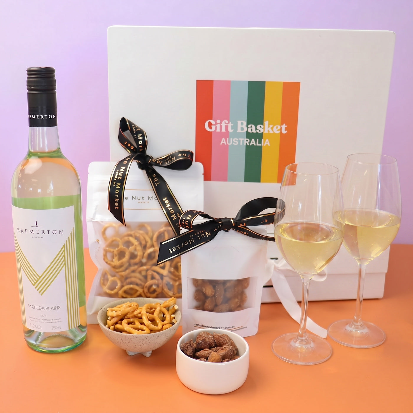 Gift basket with wine, pretzels, and snacks on a lilac background