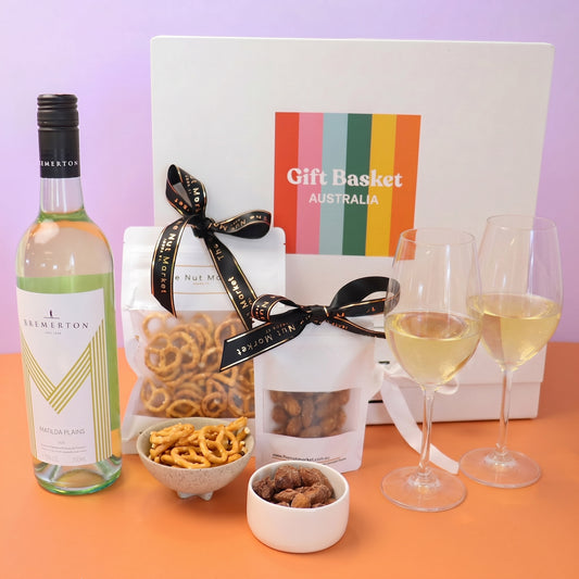 Gift basket with wine, pretzels, and snacks on a lilac background