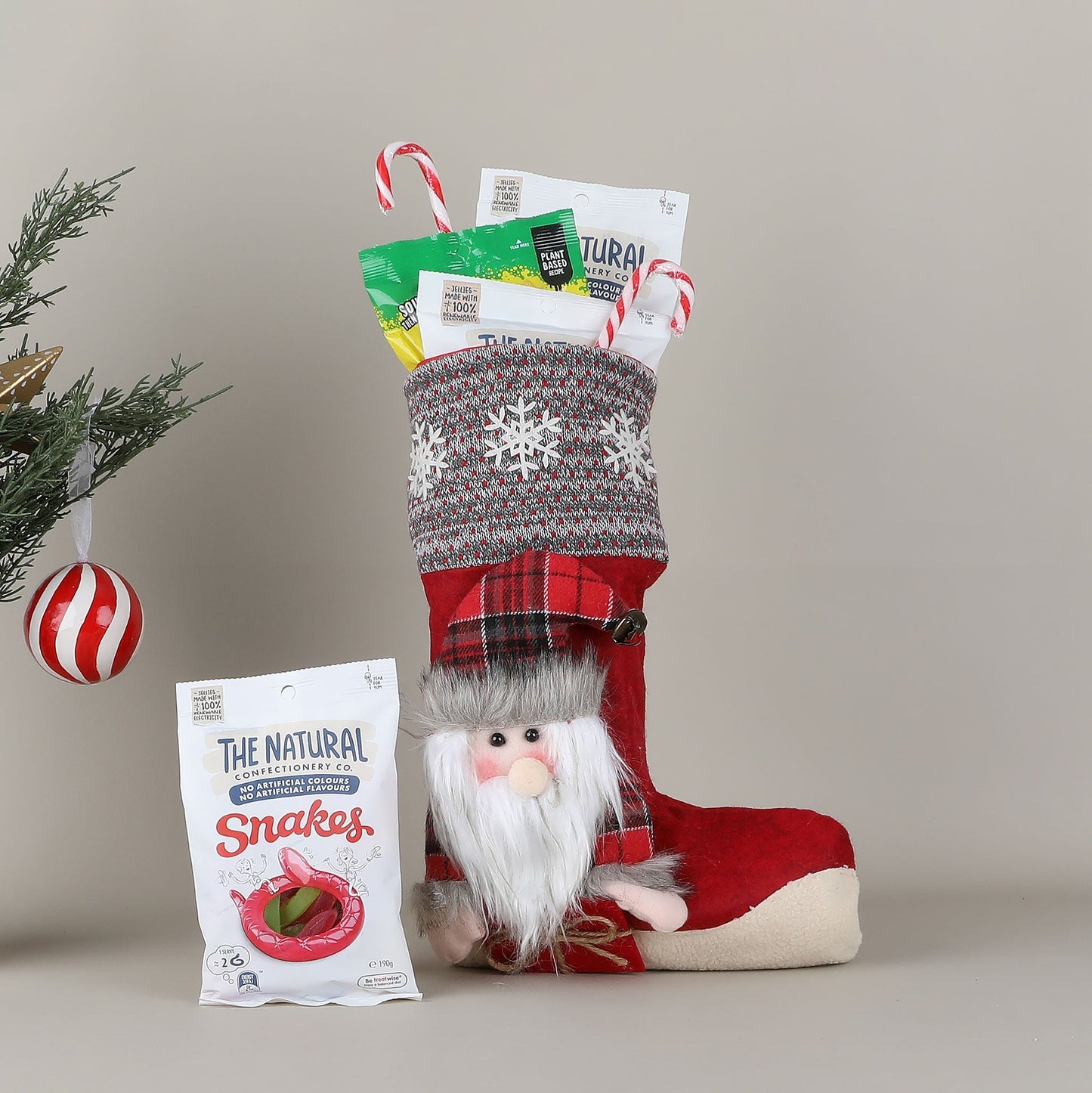 Red Christmas stocking with a gnome on it and a packet of snakes on a neutral background
