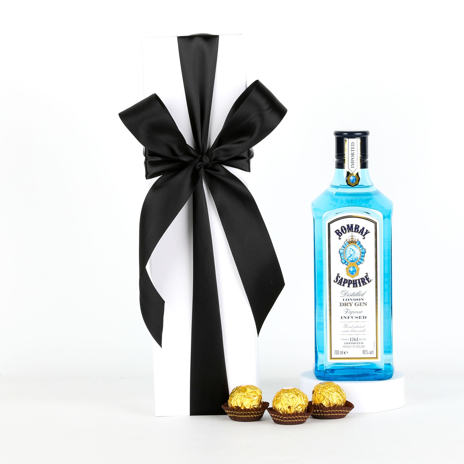 Bottle of Bombay Sapphire gin with a black ribbon and Ferrero Rocher chocolates on a white background