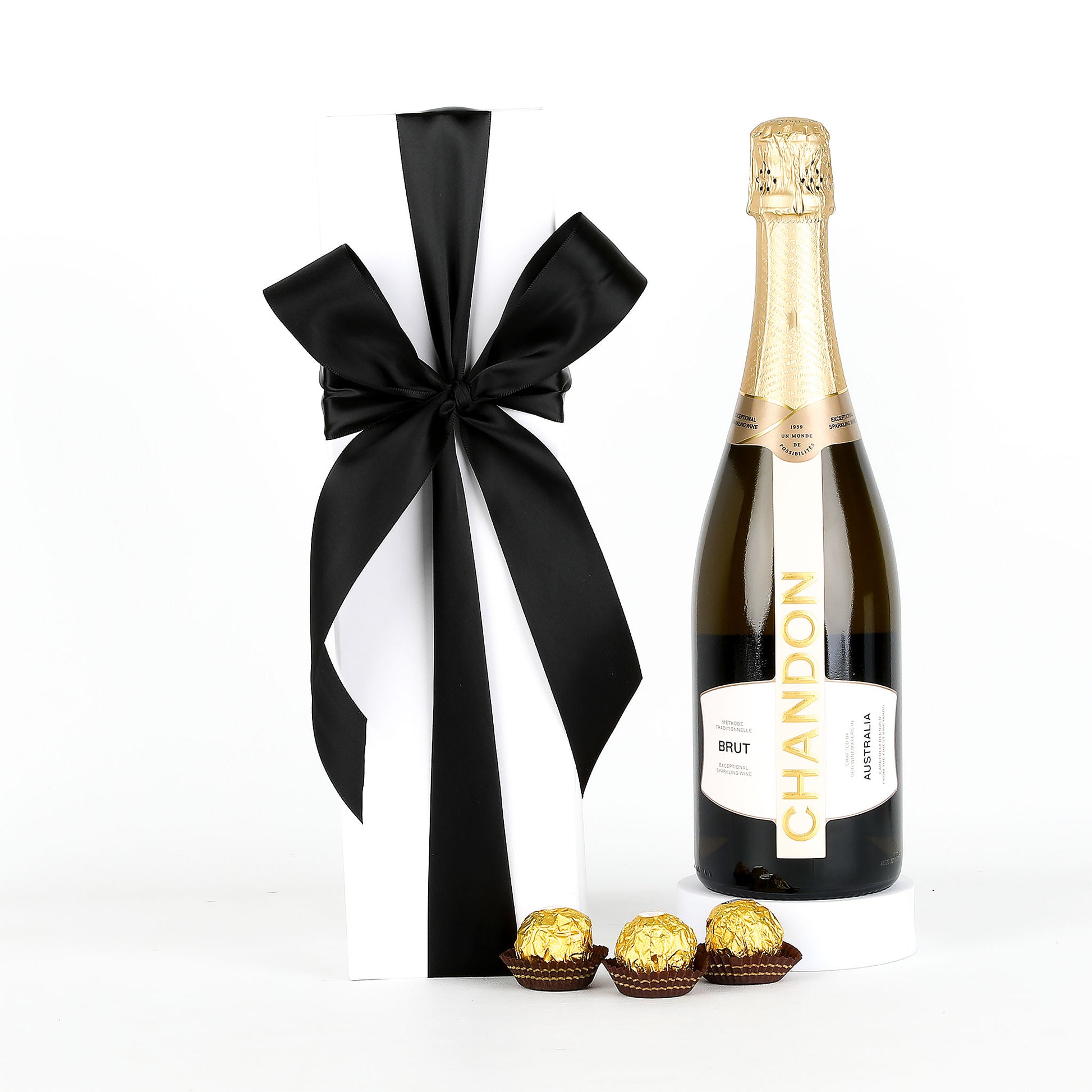 Bottle of Chandon champagne with a black ribbon and Ferrero Rocher chocolates on a white background