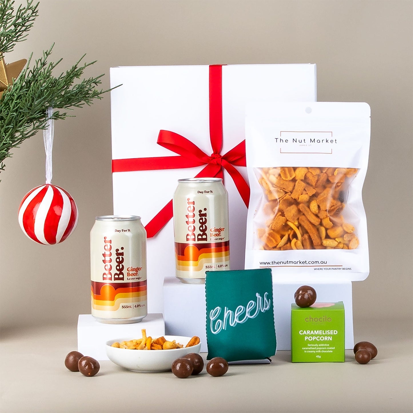 Gift set with two cans of ginger beer, & snacks on a neutral background.