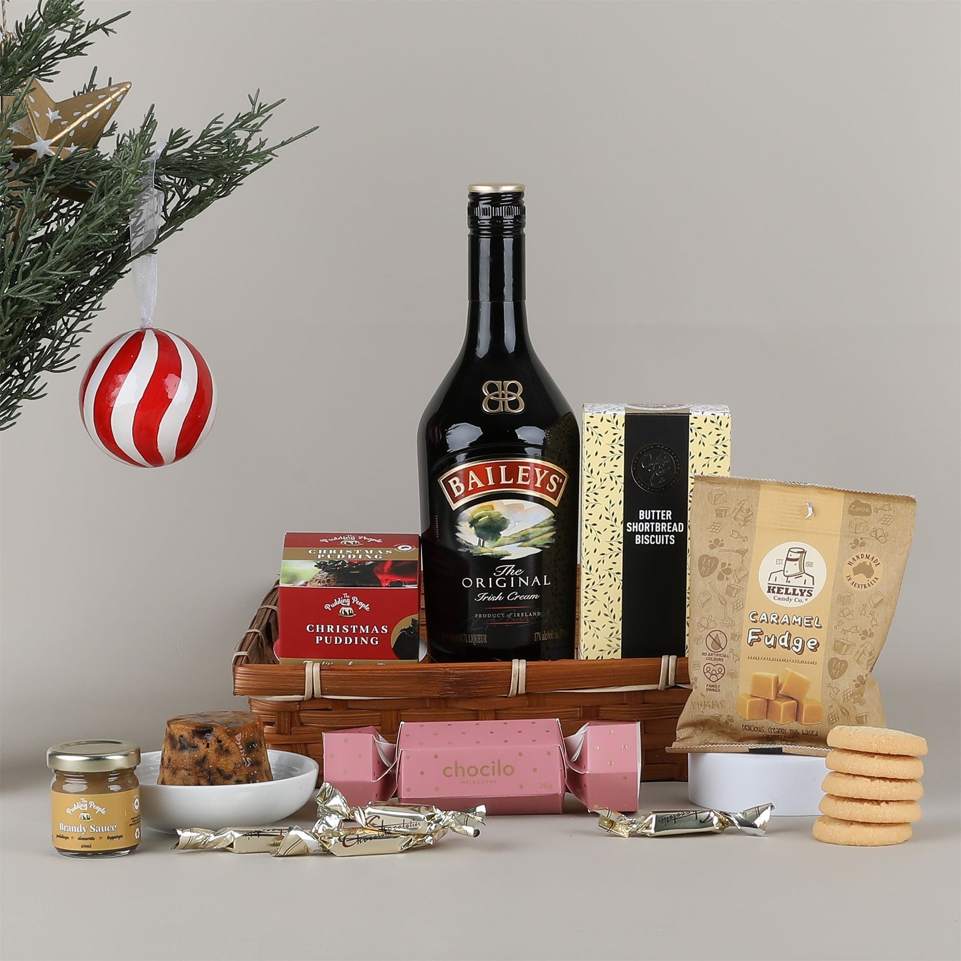 Baileys bottle with Christmas-themed items including cookies and pudding on a gray background