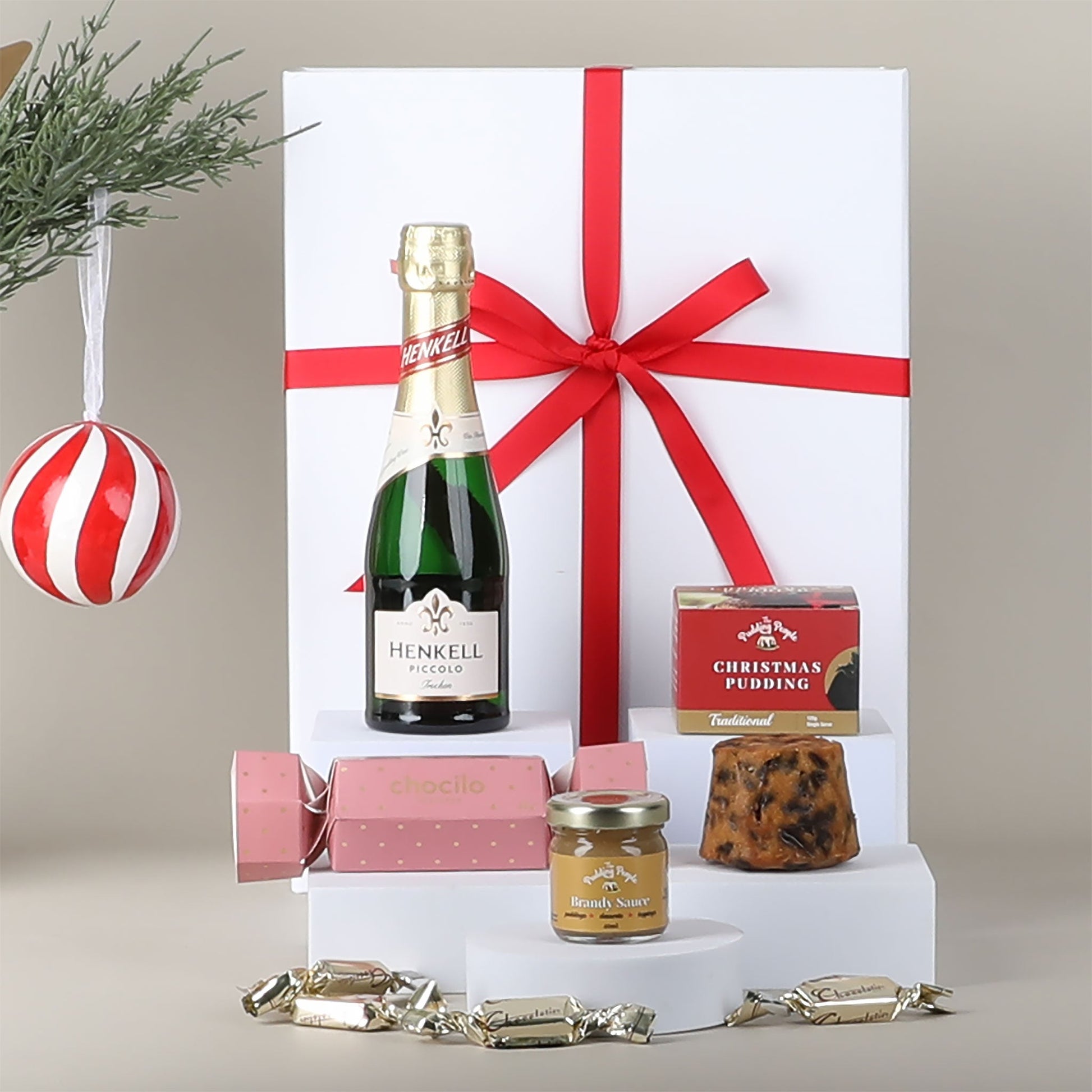 Gift set with Henkell Piccolo Sparkling Wine, Christmas pudding, and other items on a neutral background.
