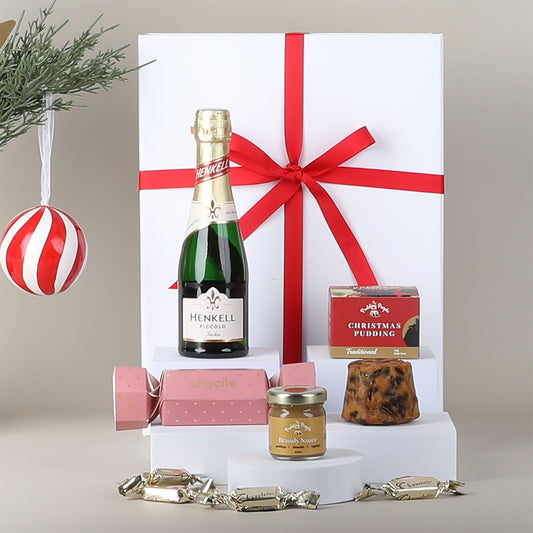 Gift set with Henkell Piccolo Sparkling Wine, Christmas pudding, and other items on a neutral background.