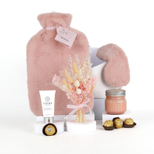 Pink hot water bottle, mittens, flowers, cream, and chocolates on a white background