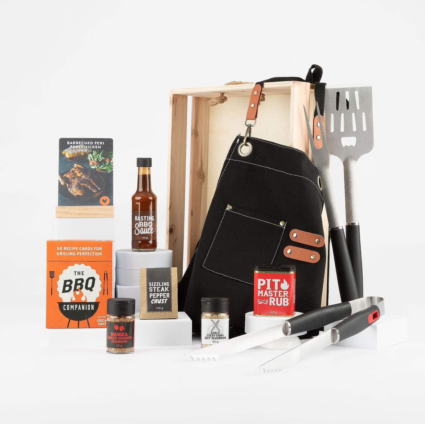 Gourmet BBQ gift set with apron, tools, and seasonings on a white background