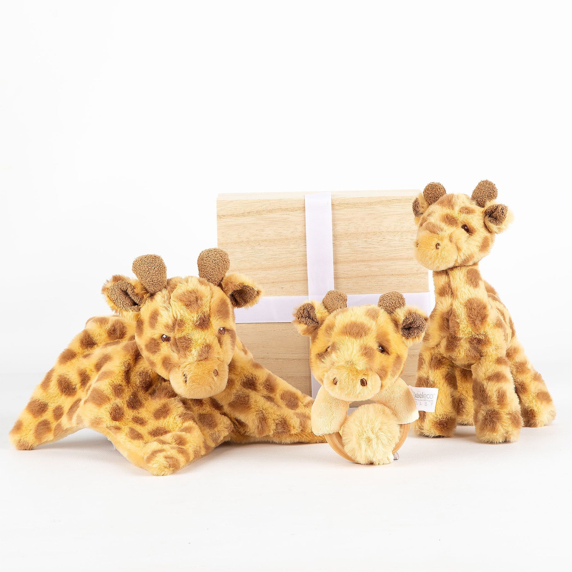 Three plush giraffe toys in front of a wooden gift box on a white background
