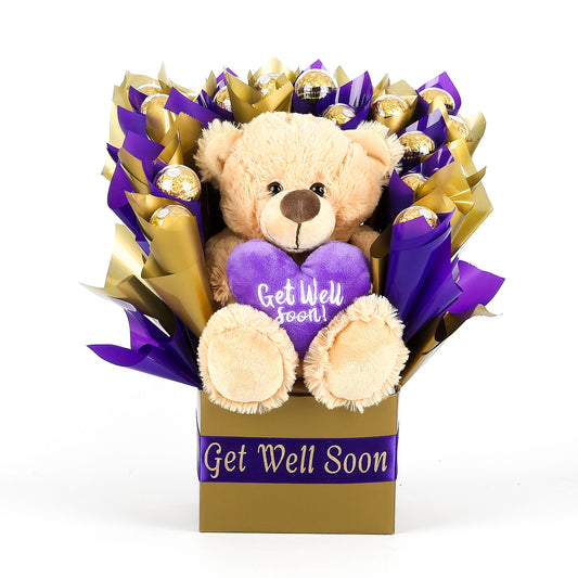 Teddy bear with a 'Get Well Soon' heart in a bouquet of chocolates wrapped in purple and gold.