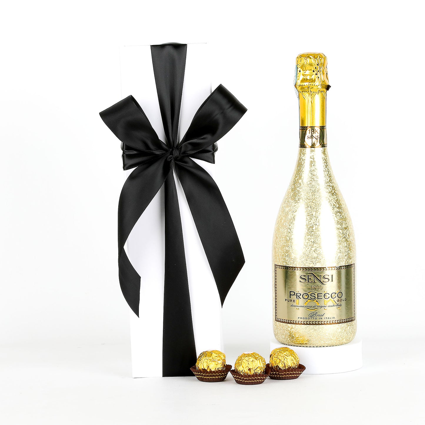 Bottle of Sensi Prosecco with a black and white ribbon, Ferrero Rocher chocolates, and a white box on a white background.