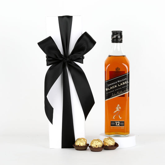 Johnnie Walker Black Label whisky bottle with a black ribbon and Ferrero Rocher chocolates on a white background