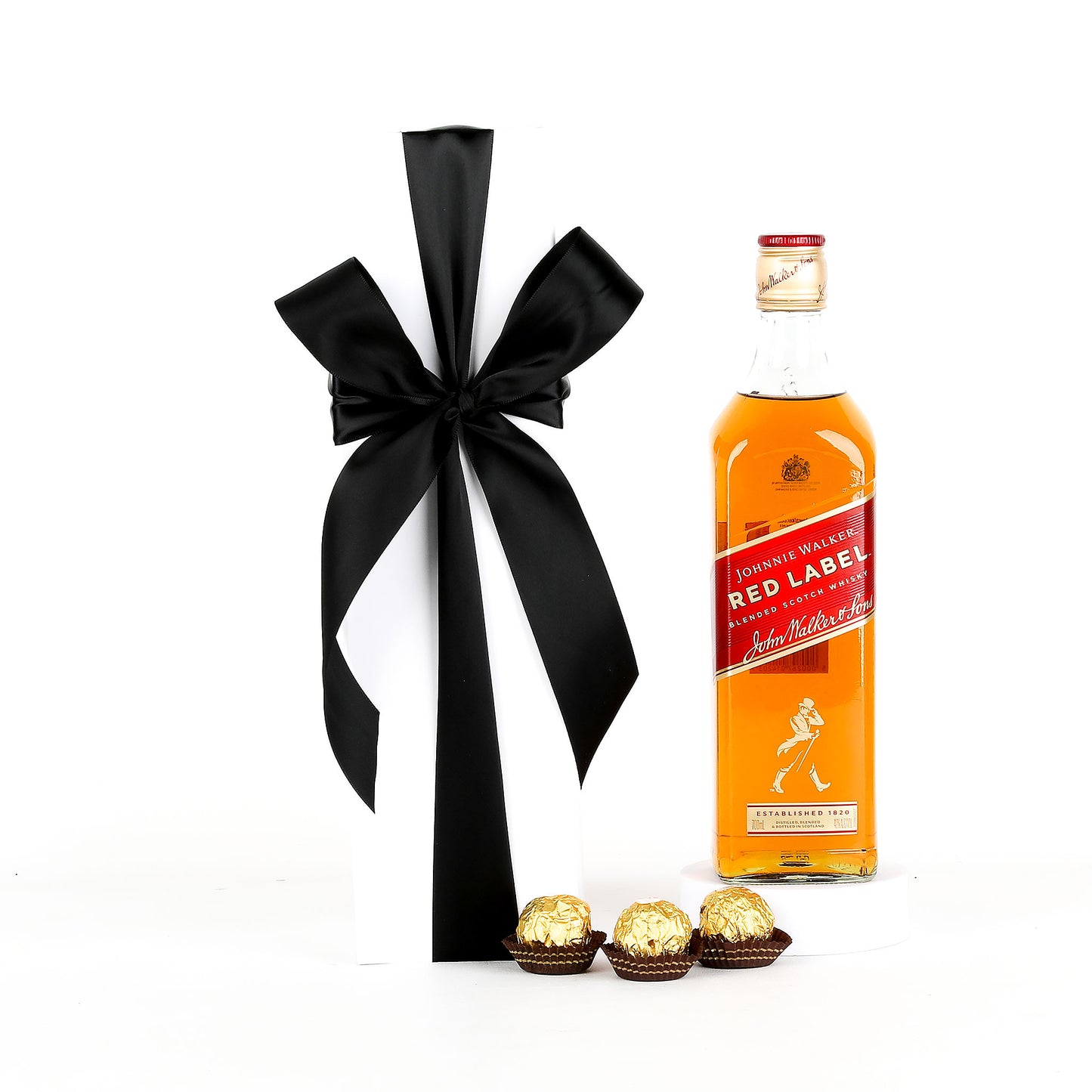 Johnnie Walker Red Label whisky bottle with a black ribbon and Ferrero Rocher chocolates on a white background