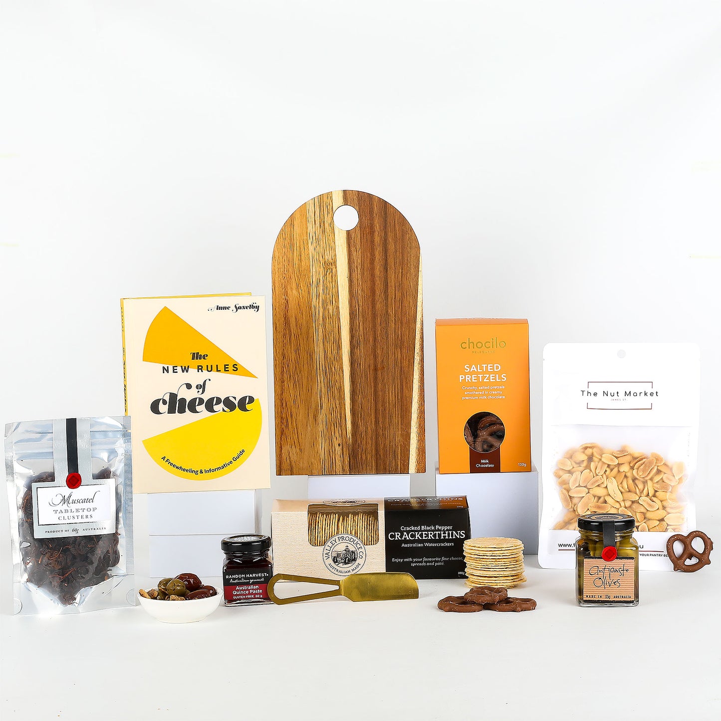 Collection of gourmet food items including a wooden cutting board, cheese book, and various snacks on a white background.