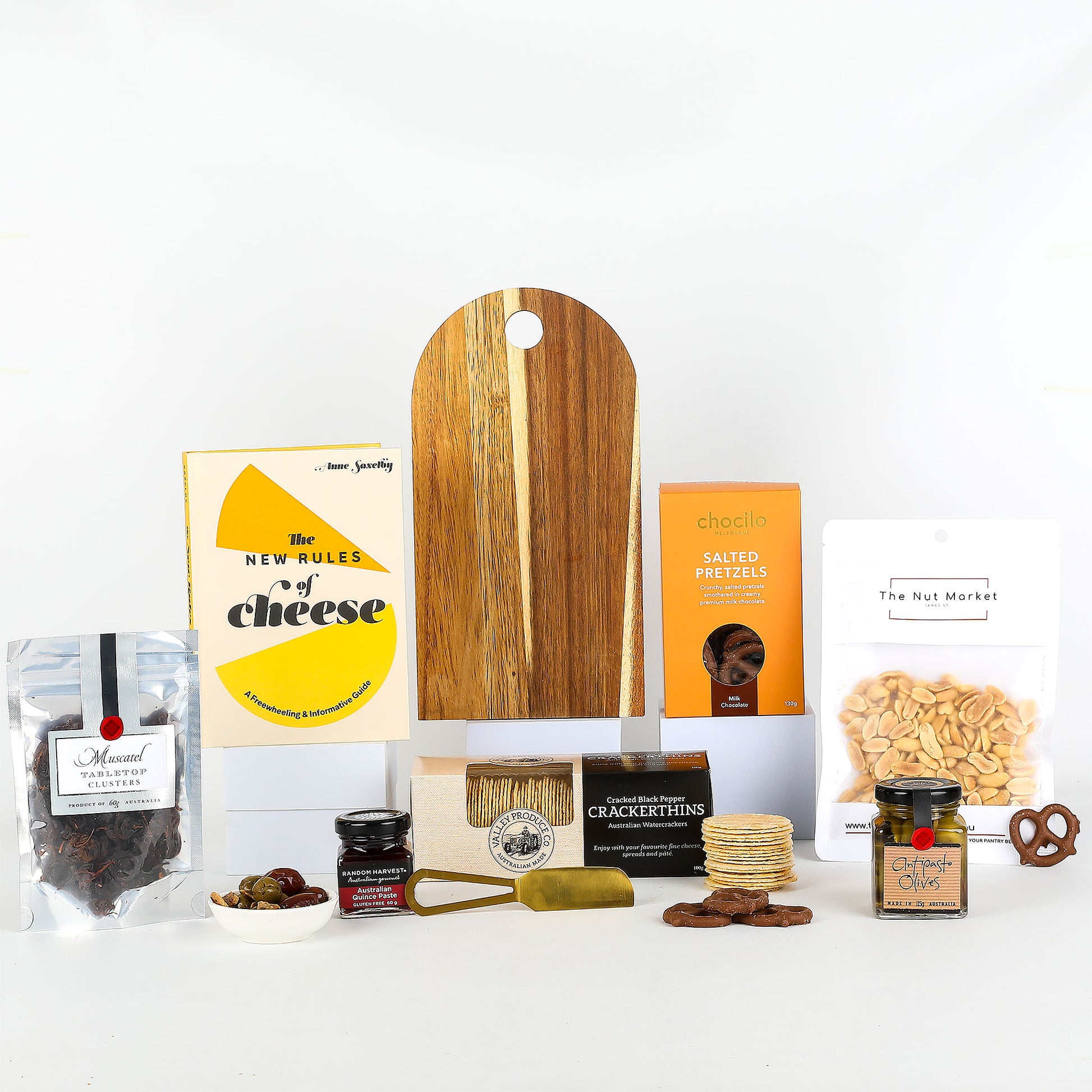 Collection of gourmet food items including a wooden cutting board, cheese book, and various snacks on a white background.