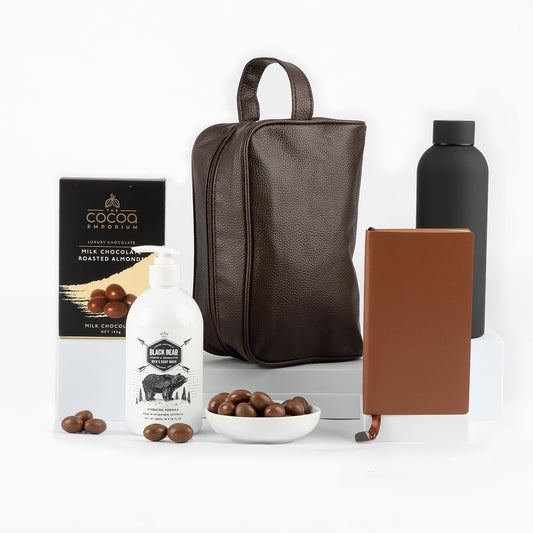 Collection of items including a leather -look bag, bottle, and chocolates on a white background
