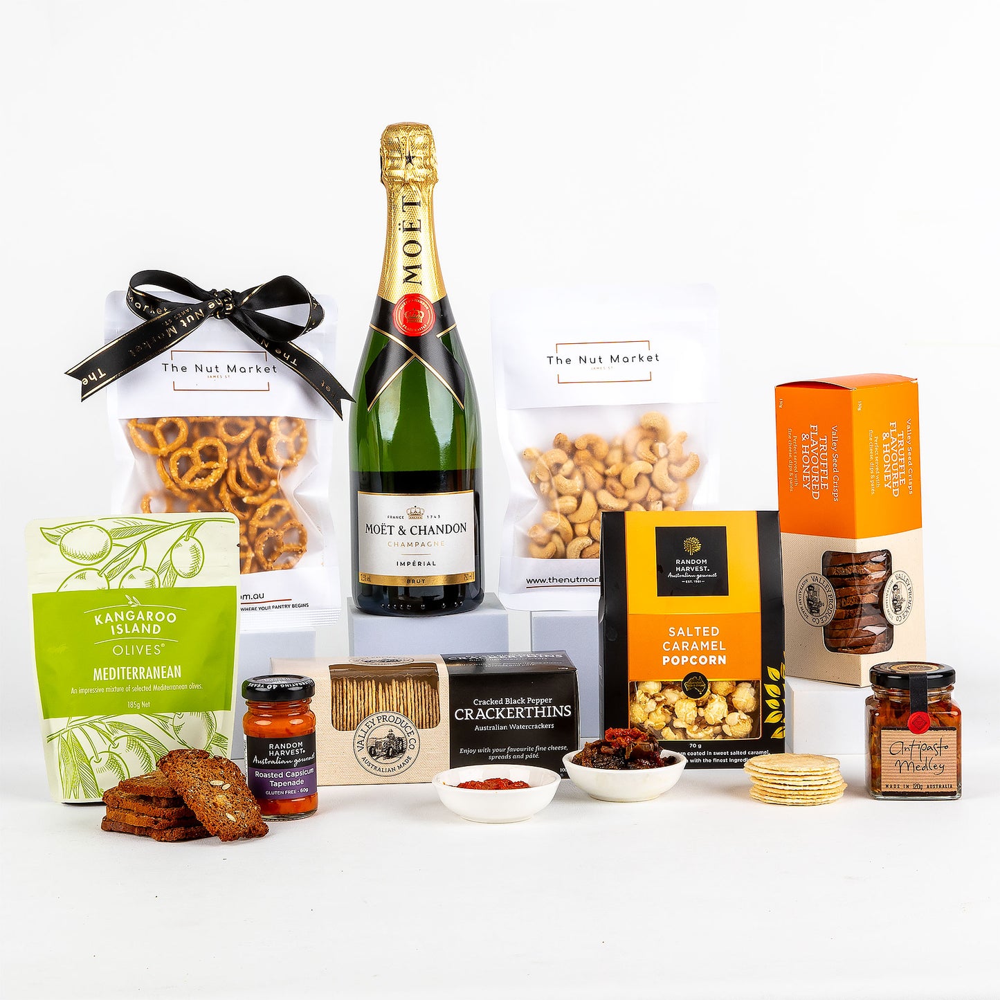 Assorted gourmet food items including a bottle of champagne, nuts, crackers and gourmet treats on a white background.