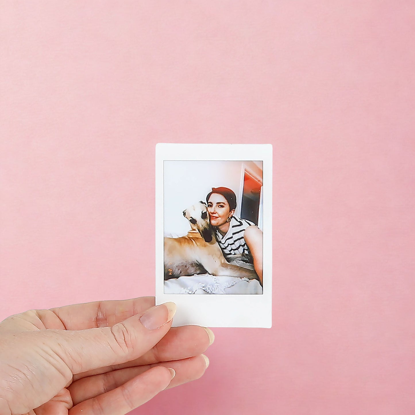 Hand holding a small photo of a woman with a dog against a pink background