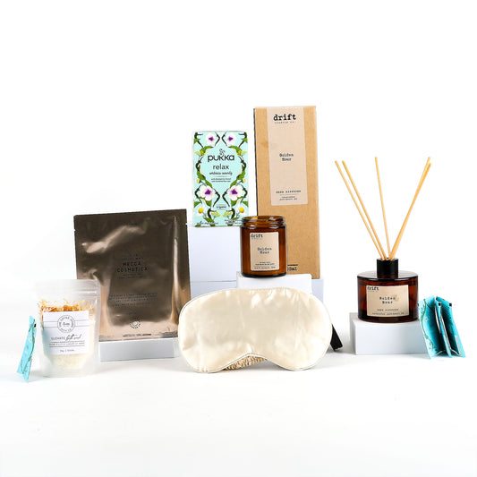 Collection of wellness products including a sleep mask, candle, and diffuser on a white background